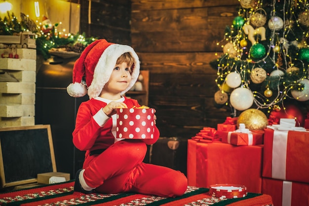 写真 冬の服を着た子供は子供のためのクリスマスツリーメリークリスマスの近くのサンタについて考えます