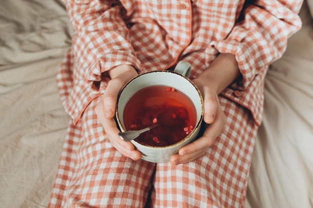 A child dressed in red plaid pajamas holds a mug of berry tea in his hands