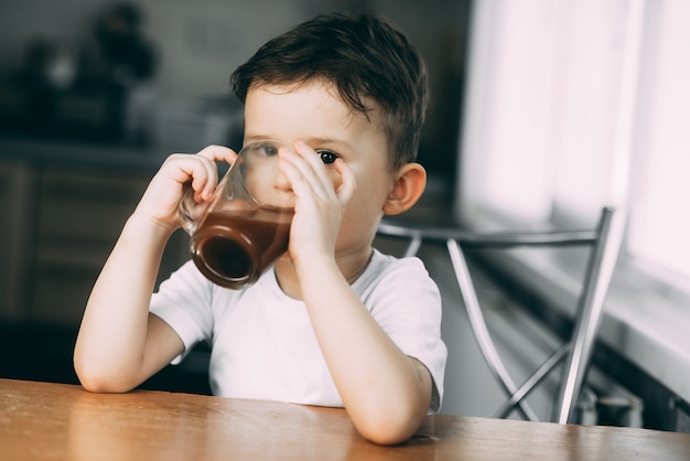 A child drinks cocoa in the kitchen or hot chocolate sweet, daylight