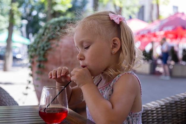 Child drinks a drink on the summer terrace under natural light. Real people.