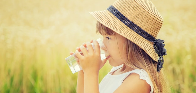 子供が畑の背景で水を飲む。