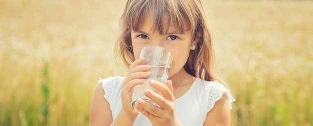 A child drinks water on the background of the field. 