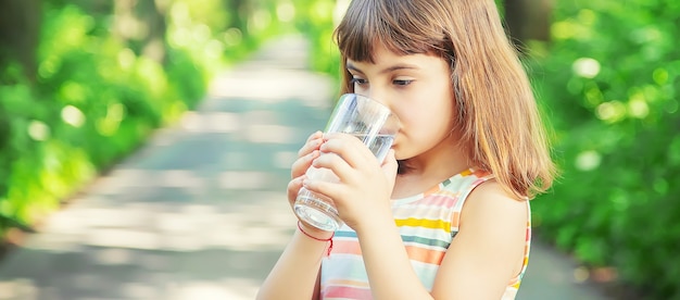 Ребенок пьет воду из стакана на природе