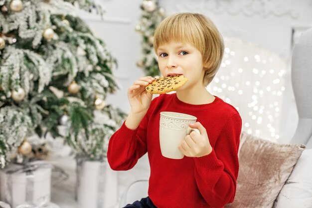 Bambino che mangia i biscotti di natale e che beve latte.