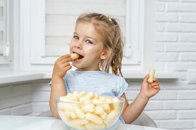 Photo child eating corn sticks at the kitchen table