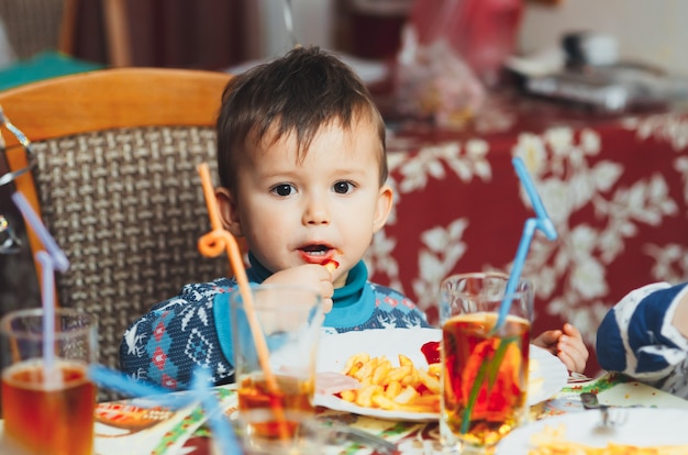 青いセーターで熱心に誕生日パーティーで手でフライドポテトを食べる子供