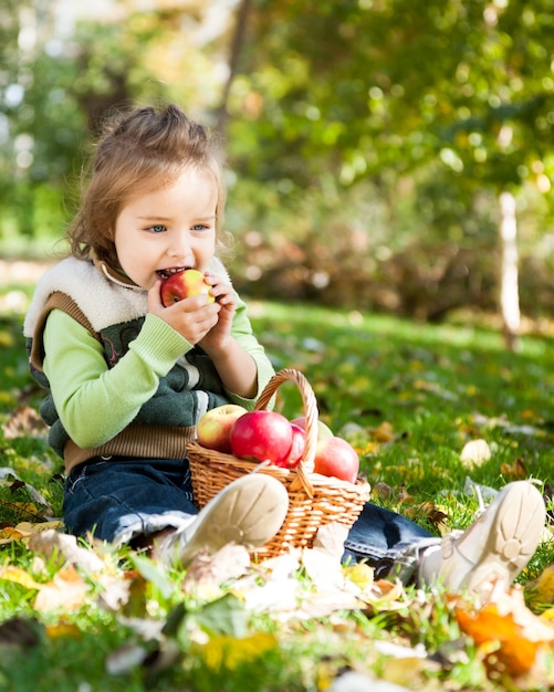 秋の公園で赤いリンゴを食べる子供