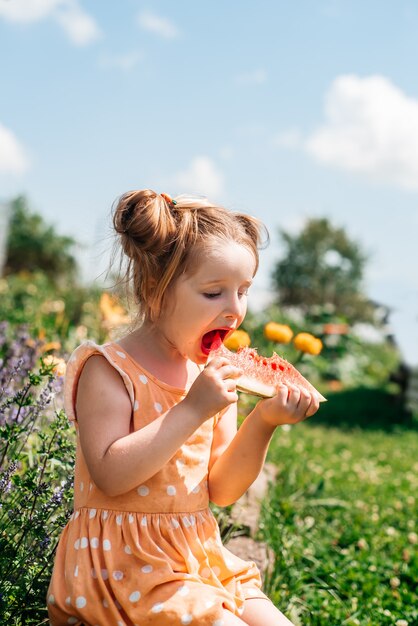 庭でスイカを食べる子供。子供たちは屋外で果物を食べます。ヘルシースナック