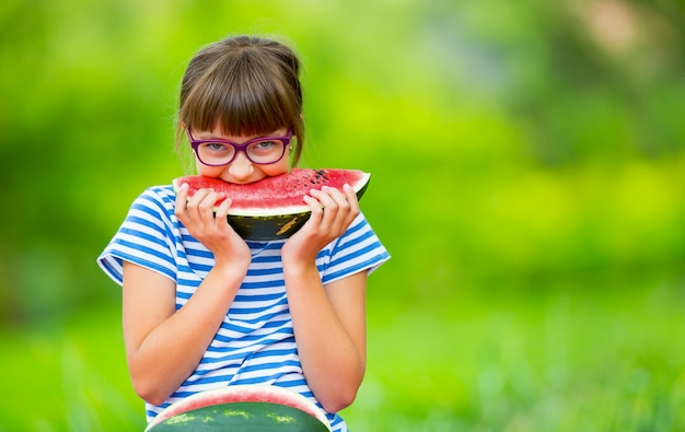 スイカを食べる子供。子供たちは庭で果物を食べます。スイカのスライスを保持している庭の10代前の女の子。スイカを食べる幸せな女の子の子供。ガスと歯のブレースを持つ女児。