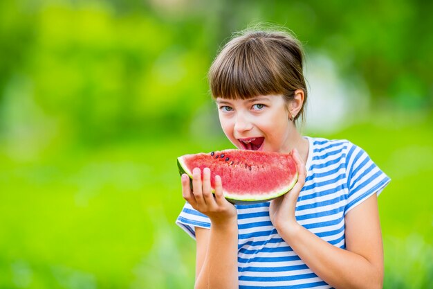 Bambino che mangia anguria ragazza pre-adolescente in giardino con in mano una fetta di anguria ragazza felice capretto ea...