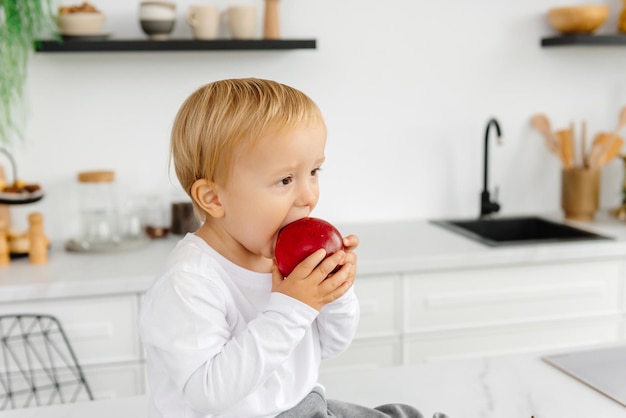 Ребенок ест яблоко на завтрак, сидя на кухне, здоровое питание для всей семьи