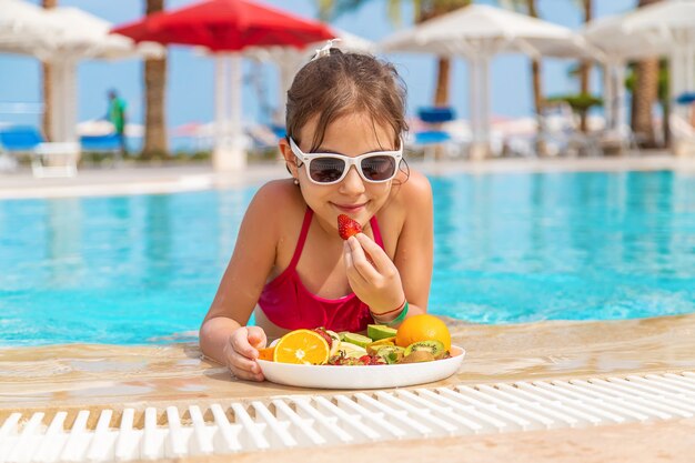 The child eats fruit near the pool