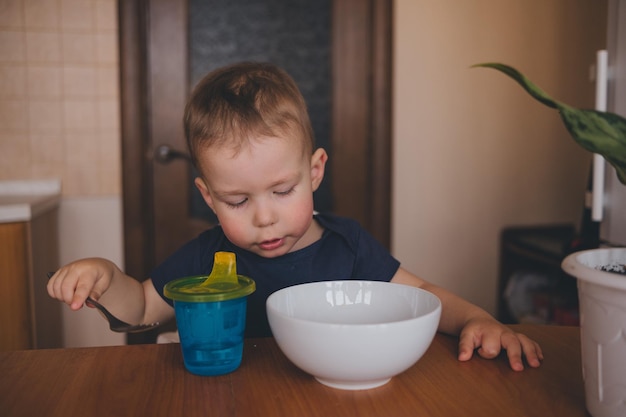 子供が台所のテーブルで白いカップからパスタを食べる