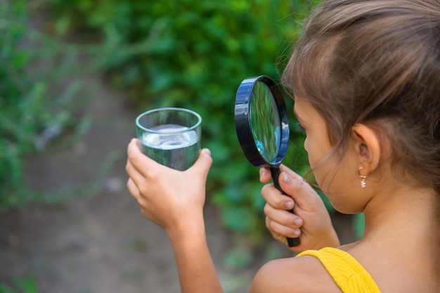 The child examines a glass of water with a magnifying glass. Selective focus.