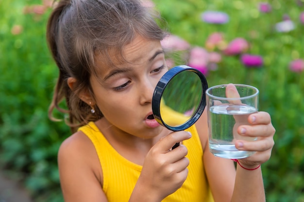 The child examines a glass of water with a magnifying glass. Selective focus.