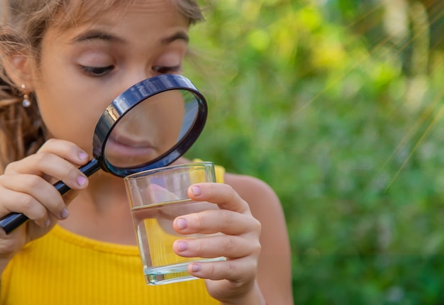 The child examines a glass of water with a magnifying glass. Selective focus.