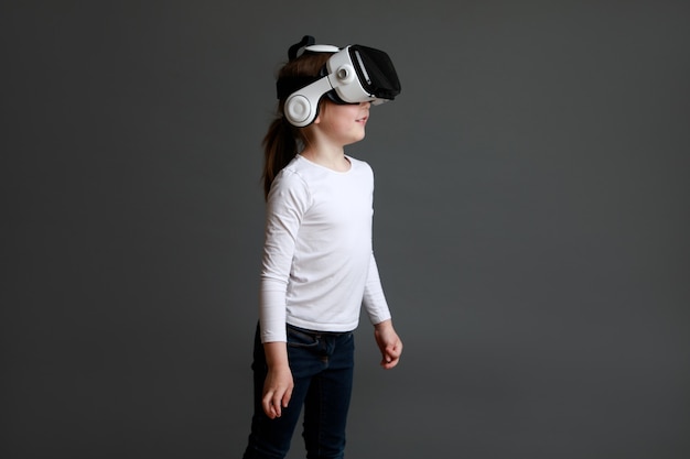 Child experiencing virtual reality on grey surface. Surprised cute girl looking in VR glasses.