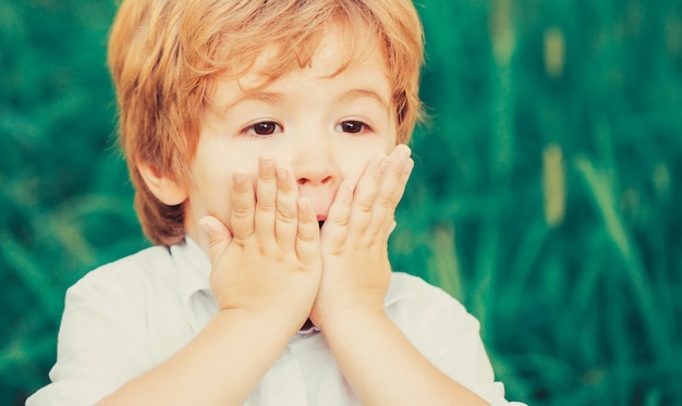 顔に手を当てて驚きを表現する子供。驚いたり驚いたりする子供の男の子の笑顔。ショックを受けて驚いた少年。