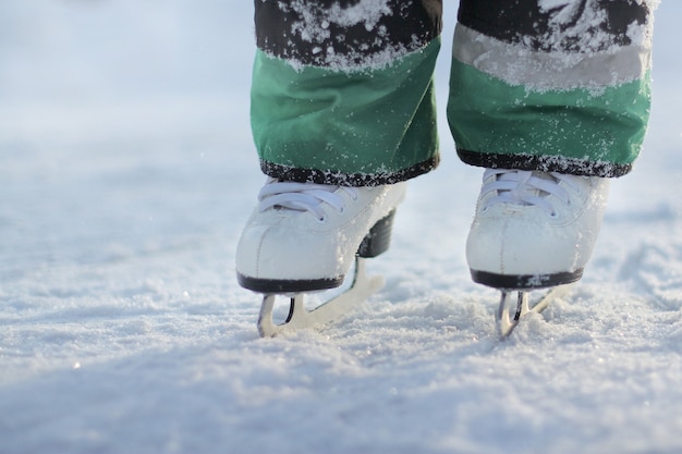 Foto i piedi del bambino in pattini bianchi stanno sul ghiaccio. pattinaggio su ghiaccio in una gelida giornata invernale.