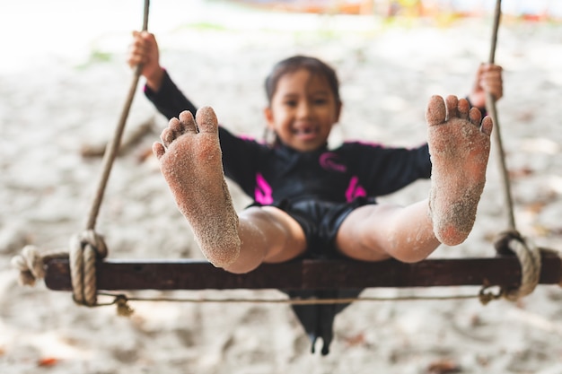 Child feet with sand while she playing on a swing at the beach near the sea in summer vacation