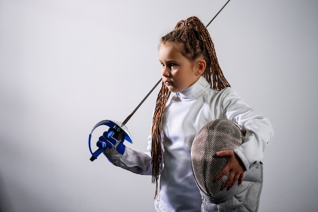 A child in a fencing costume is holding an epee. Girl learning fencing