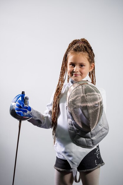 A child in a fencing costume is holding an epee. Girl learning fencing