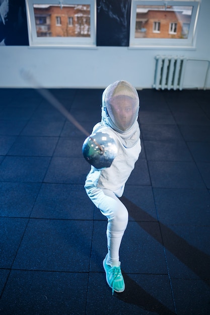 Foto bambino in costume da scherma e maschera, con una spada, scuola di scherma