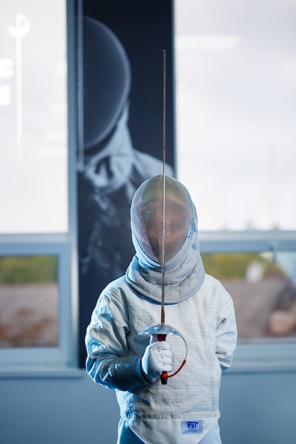 Child in a fencing costume and mask, with a sword, fencing school