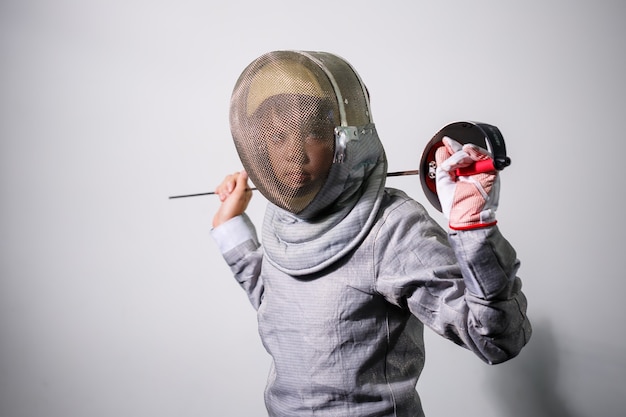 Foto bambino in una tuta da scherma con una spada in mano in studio. le ragazze praticano e praticano la scherma. sport, stile di vita sano.