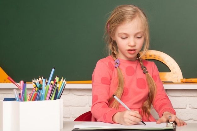 Child from elementary school sitting at table in classroom at primary school writing or drawing in n