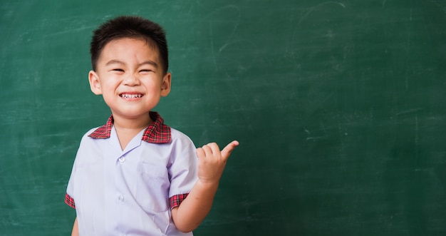 Child from kindergarten in student uniform smiling on green school blackboard