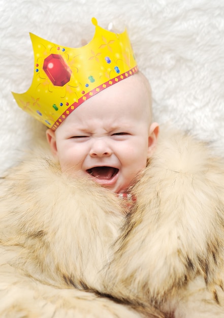 Ребенок в меховой накидке и короне на белом фоне. плач ребенка
