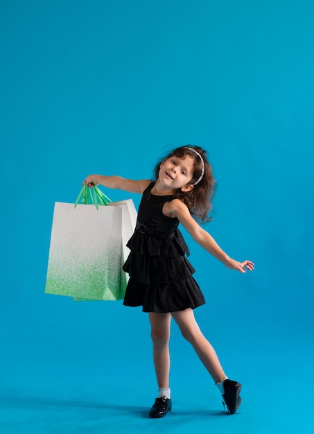Девочка в черном платье с бумажными пакетами на простом фоне. Магазин для скидок