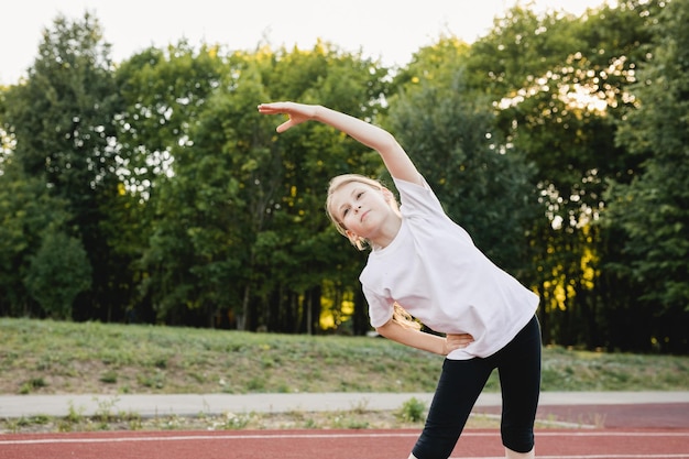 写真 公共公園のスポーツトラックで走る前に屋外でウォーミングアップトレーニングをしている子供の女の子