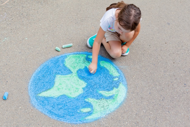 The child girl draws a planet, globe with a map of the world with chalk on the asphalt