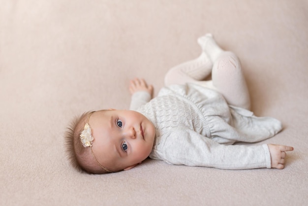 Una bambina con un vestito giace sulla schiena su uno sfondo beige e guarda