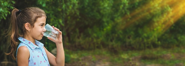 La ragazza del bambino beve l'acqua da un bicchiere messa a fuoco selettiva