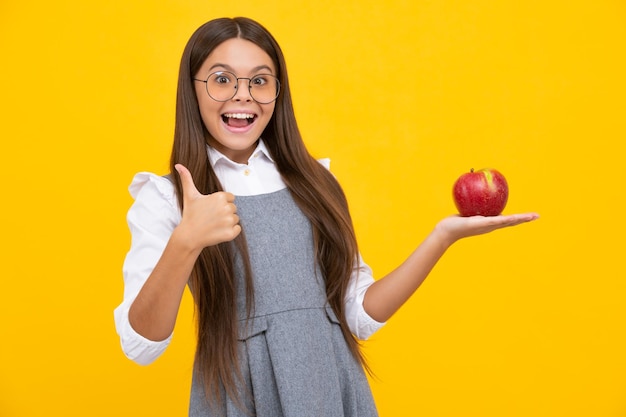 Child girl eating an apple over isolated yellow background tennager with fruit happy girl face positive and smiling emotions