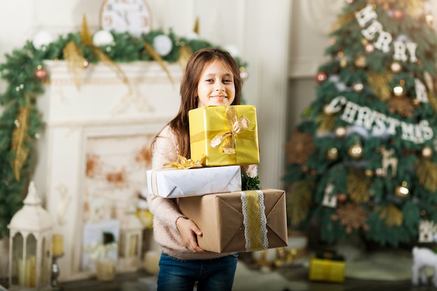 Child girl in front Christmas tree with gift boxes.