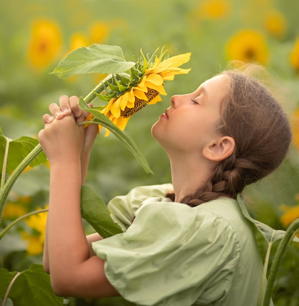 child girl in a green dress stands in a field with sunflowers and holds a sunflower in her hands