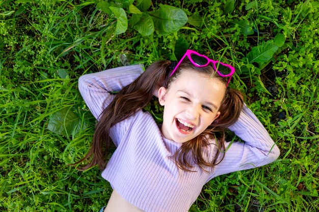 선글라스를 끼고 푸른 풀밭에 있는 어린 소녀는 주말과 방학의 개념인 행복으로 거짓말을 하고 웃거나 웃는다