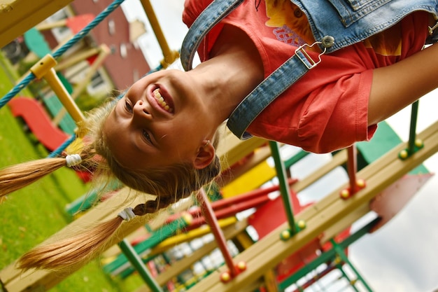 Foto bambina appesa a testa in giù nel parco giochi. ragazza sorridente dell'adolescente che gioca ad una costruzione di sport.