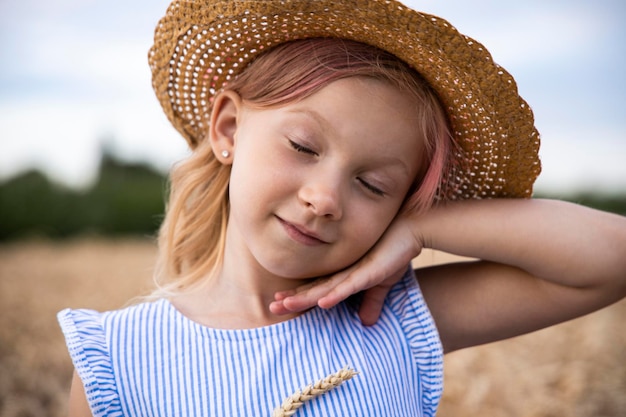 麦畑を背景にポーズをとる帽子をかぶった子供の女の子