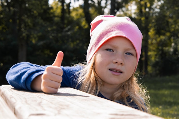 Child girl in a hat showing thumbs up on the street