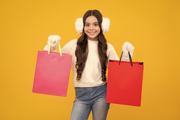 Child girl hold shopping bag enjoying sale isolated on yellow\
background portrait of teenager girl is ready to go shopping happy\
face positive and smiling emotions of teenager girl