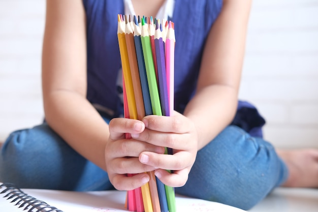 Child girl holding many color pencils sitting on floor