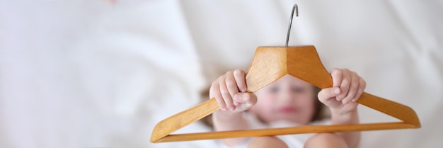 Child girl holding wooden hange closeup choosing clothes hanger