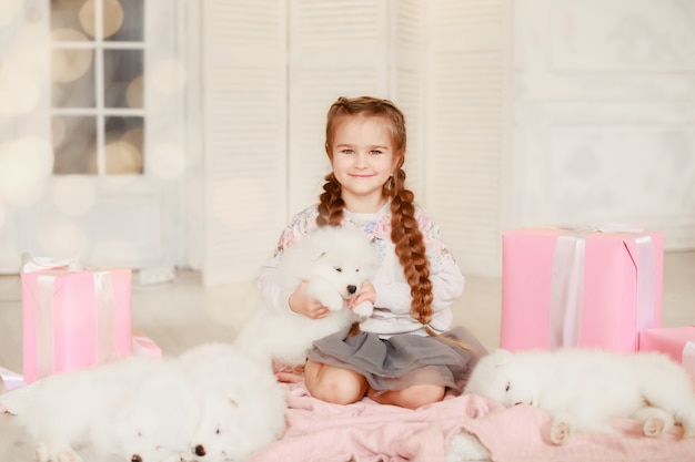 Child girl is holding puppy on her hands near pink the gift boxes