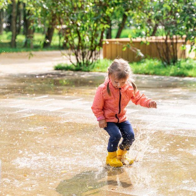 Child girl jumping and playing in a puddle after rain