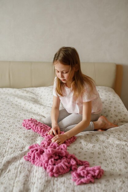 Child girl knits from yarn sitting on the bed